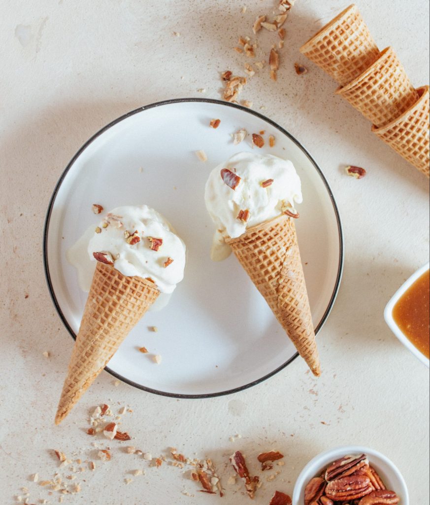 A food photograph of two vanilla ice cream cones on a round white plate