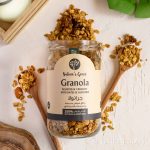 A photo of a granola jar open with its contents spilling out of it and two spoonfuls of granola