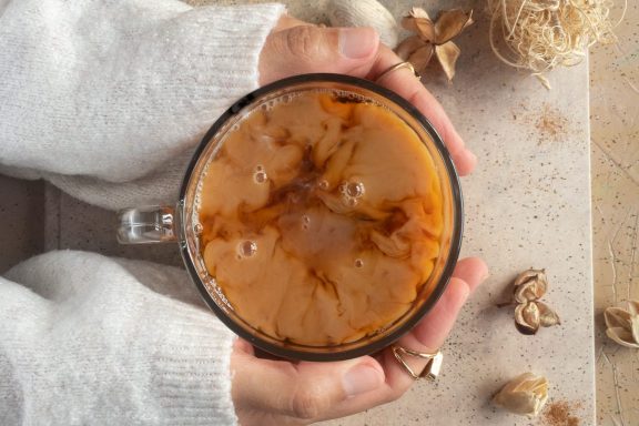 A food photograph of two hands holding a cup of chai tea